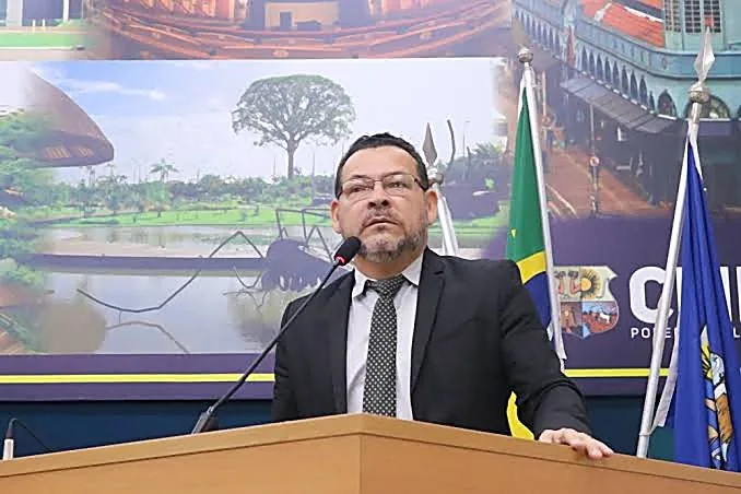 Mauro Freitas discursando na tribuna, com o brasão e as bandeiras ao fundo